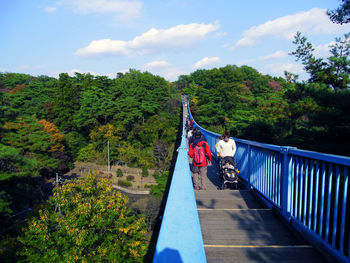 People on bridge amidst trees against sky