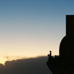 Silhouette man holding sculpture against clear sky during sunset