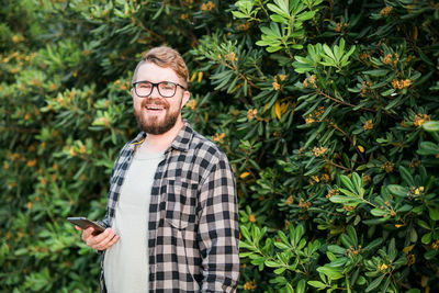 Portrait of smiling man holding smart phone in front of plant