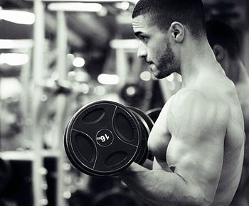 Side view of shirtless man weightlifting in gym