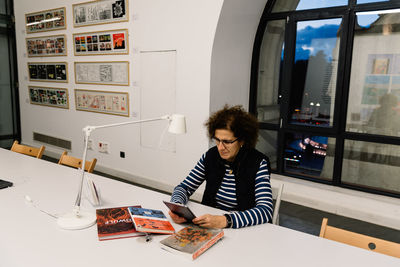 Mature woman using digital tablet by books on desk