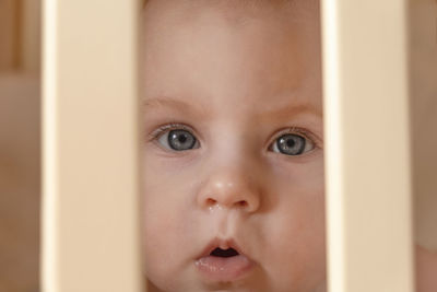 Close-up face of a crying cute baby between the bars of the crib. little baby girl with tearful eyes