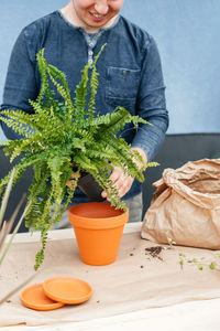 A young male florist and gardener transplants a homemade fern into a clay pot. hobbies