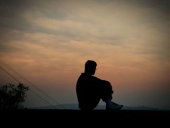 Silhouette of man sitting against sky during sunset