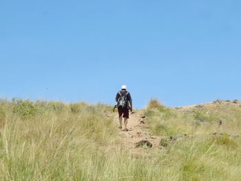 Rear view of man walking on field against clear sky