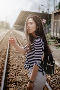 Young woman looking away while standing on railroad track