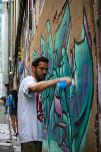 Young man standing against graffiti wall in city