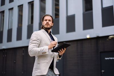 Professional employee writing notes on tablet while standing near the office building