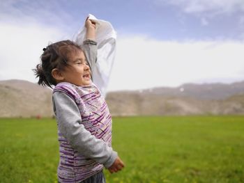 Cute girl holding fabric while standing on field against sky