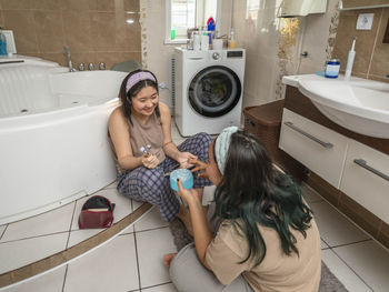 Asian laughing beauties begin morning routine with acne treatment and facial massage in bathroom