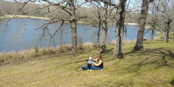 People sitting on grass by trees and lake