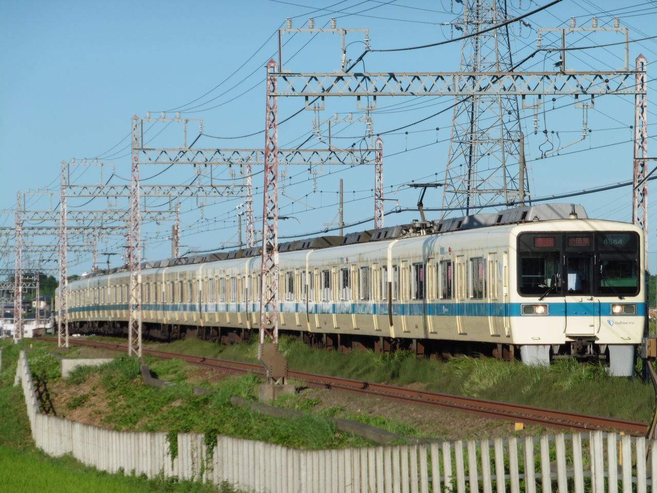 architecture, built structure, building exterior, grass, clear sky, tree, transportation, blue, sky, day, railroad track, outdoors, sunlight, city, rail transportation, no people, public transportation, fence, bare tree, building