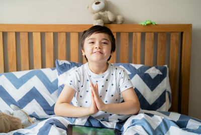 Portrait of smiling boy sitting on bed at home