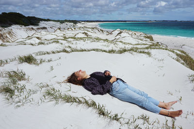 Woman lying on sand at beach against sky