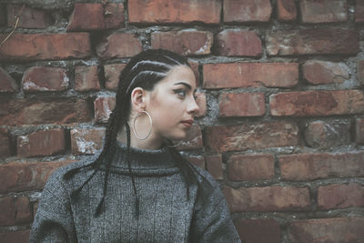 Young woman looking away against brick wall