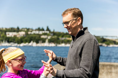 Father and daughter playing while standing by retaining wall against sky