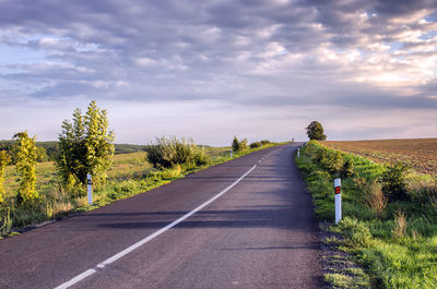 Empty road amidst field against cloudy sky