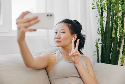 Side view of young woman using mobile phone while sitting on bed at home