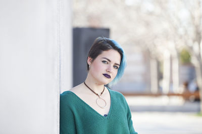 Portrait of young woman standing against wall