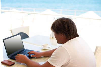 Side view of man using laptop on table against window