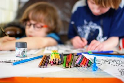 View of colored pencils on table with boys drawing in background