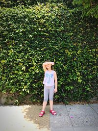 Full length of girl covering eyes while standing against ivy