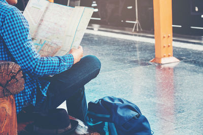 Low section of man with map sitting at railroad station platform