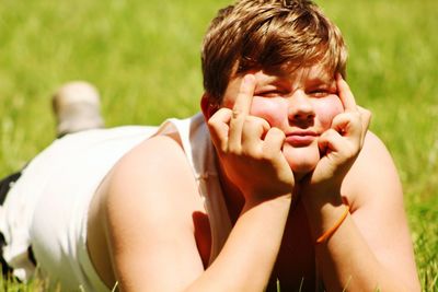 Boy showing middle fingers while lying at park on sunny day