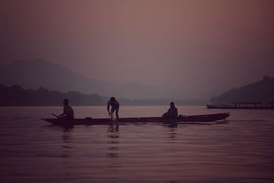 Men on boat at river against sky during sunset