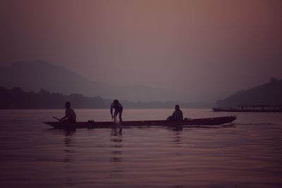 Men on boat at river against sky during sunset