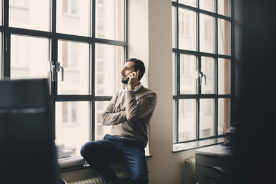 Male entrepreneur talking on smart phone by window in creative office