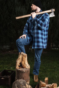 Lumberjack holding axe while standing by log at forest