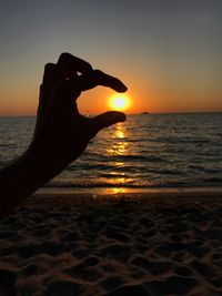 Close-up of silhouette hand against sea during sunset
