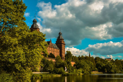 Trees and castle by river against sky