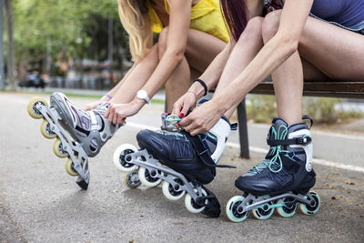 Hands of women tying lace of inline skates sitting on bench