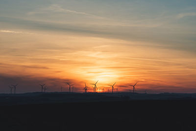 Silhouette wind turbines on land against sky during sunset