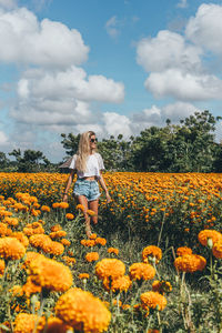 Woman standing amidst yellow flowers on field against sky