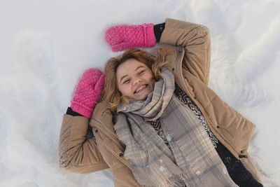 Blonde caucasian girl with pink mittens lies on the snow enjoying winter. happy joyful winter