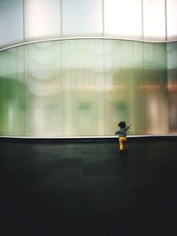 Rear view of a toddler girl walking in front of a glass window