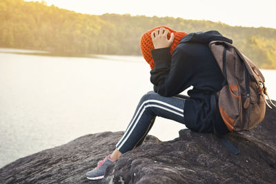 Young woman sitting on rock by lake