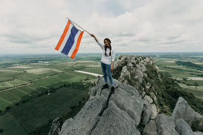 Woman standing on rock holding flag against sky