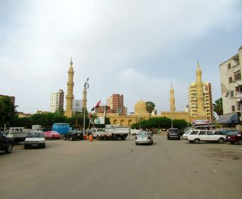 Cars on road by buildings in city against sky