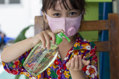 Portrait cute girl wearing mask using hand sanitizer outdoors