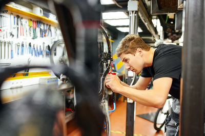 Side view of concentrated male master pumping tyre of bike wheel using inflating gun in workshop