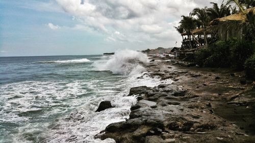 Waves splashing on rocks at shore against sky