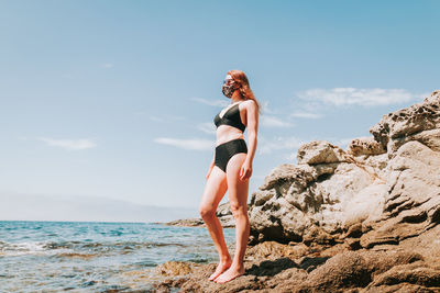 Full length of woman standing on rock by sea against sky