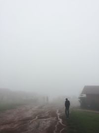 Rear view of man walking on field during foggy weather