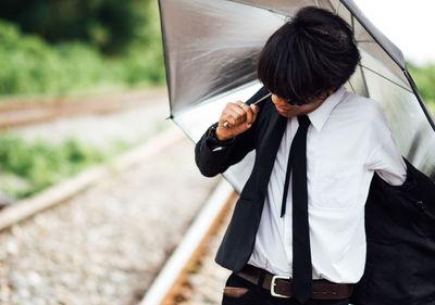 Young man getting dressed and holding umbrella while standing on railroad track