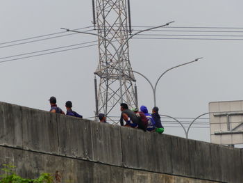 Low angle view of people on electricity pylon against sky