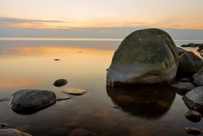 Rocks in sea against sky during sunset